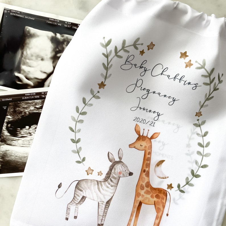 May include: A white fabric bag with a green leafy border and gold stars. The text "Baby Chabbings Pregnancy Journey 2020/21" is printed in black cursive font. A watercolor illustration of a giraffe and zebra is in the center of the bag.