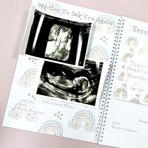 May include: A white pregnancy journal with a rainbow and star pattern. The journal has a spiral binding and includes a section for ultrasound photos. The text "We Got To See You Again!" is printed on the cover.