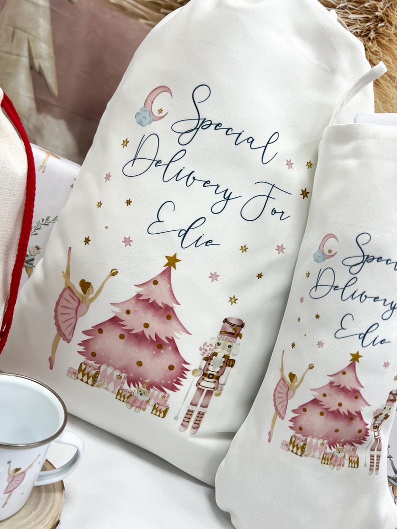 May include: Two white fabric gift bags with pink and gold illustrations of a ballerina, a Christmas tree, and a nutcracker. The bags have the text "Special Delivery For Edie" on them.