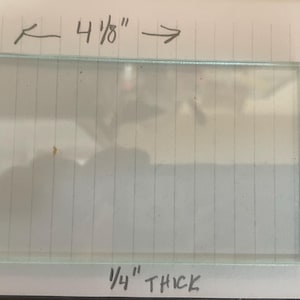 Puede incluir: Un trozo rectangular de vidrio transparente, de 10,5 cm de largo, 5,7 cm de ancho y 0,6 cm de grosor. El vidrio transparente podría ser un pequeño cristal de ventana o un artículo similar.