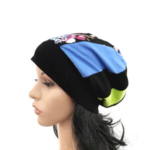 Può includere: Un berretto nero con un design patchwork. Il patchwork include un quadrato blu, una stampa floreale e una sezione verde. Il berretto è indossato da una persona con capelli neri e carnagione chiara.