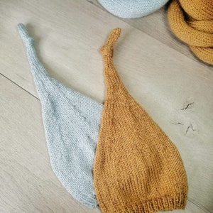 Könnte beinhalten: Zwei gestrickte Baby-Mützen, eine hellblau und eine senfgelb. Die Mützen liegen auf einer Holzoberfläche.