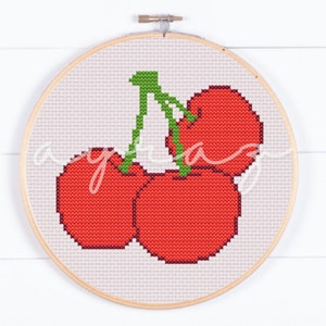 May include: A cross-stitch embroidery hoop featuring a design of three red cherries with green stems.