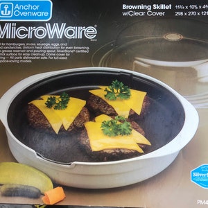 May include: White ceramic browning skillet with a clear lid. The skillet is 11 1/2 inches by 10 inches by 4 3/4 inches and is 298 mm by 270 mm by 121 mm. The skillet is shown with cooked hamburger patties and cheese slices. The packaging features the text "MicroWare" and "SilverStone" with a blue and white logo.