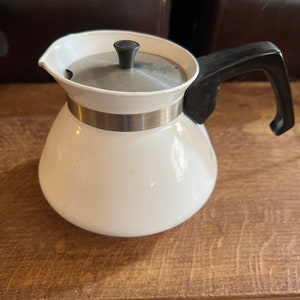 May include: White ceramic coffee pot with a black handle and lid. The pot has a silver band around the middle.