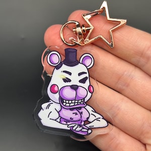 Puede incluir: Un llavero de acrílico con un personaje de oso de dibujos animados con pelaje blanco, hocico morado y sombrero de copa negro. El personaje tiene una complexión musculosa y una sonrisa amplia y dentada. Unido a un cierre metálico en forma de estrella.