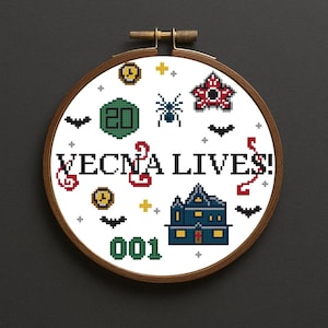 May include: Cross-stitch embroidery in a wooden hoop with the text "VECNA LIVES!". The design includes a spider, bats, a house, and other elements. The color palette includes white, black, red, green, and yellow.