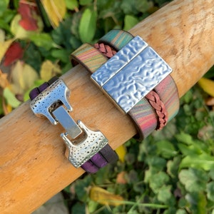 Pu&ograve; includere: Due braccialetti in pelle con chiusure argentate. Un braccialetto &egrave; multicolore con un cinturino in pelle intrecciato e una chiusura rettangolare argentata testurizzata. L'altro braccialetto &egrave; viola con una chiusura argentata testurizzata.