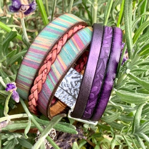 Pu&ograve; includere: Tre braccialetti in pelle impilati uno sopra l'altro. Il braccialetto superiore &egrave; di un viola intenso con un motivo floreale. Il braccialetto intermedio &egrave; di design a strisce multicolori con un cinturino in pelle intrecciato. Il braccialetto inferiore &egrave; in pelle marrone con una chiusura in metallo argentato.