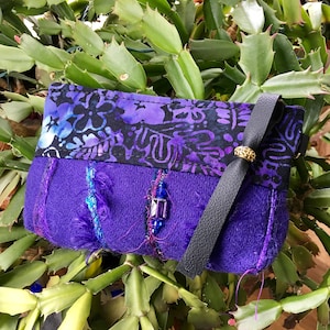 May include: A purple fabric pouch with a black strap and a floral print. The pouch has a gold accent and a blue beaded embellishment.