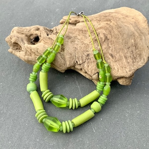 Puede incluir: Un collar de dos hilos con una variedad de cuentas verdes. El collar incluye cuentas cilíndricas, redondas y facetadas en tonos verdes claros y medios. Está ensartado en un fino cordón verde claro y tiene un cierre plateado. Aproximadamente 40 cm de largo.