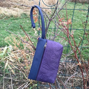 May include: A small purple leather clutch with a blue leather flap and a gold zipper. The clutch has a decorative embossed pattern and a strap with a gold clasp.
