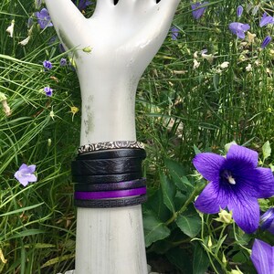 May include: A stack of black leather bracelets with a white and black patterned bracelet and a purple bracelet with a Greek key design.