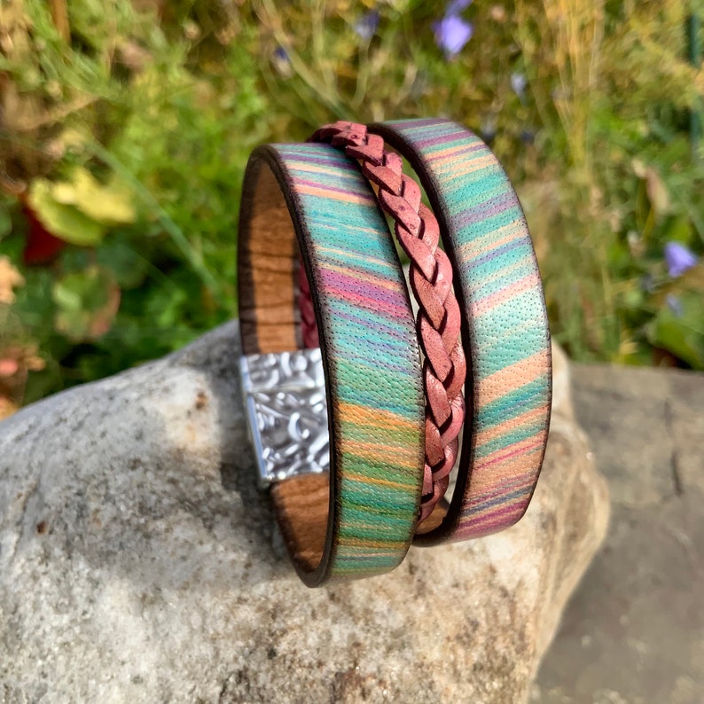 Pu&ograve; includere: Un braccialetto in pelle multistrato con un cinturino in pelle intrecciato e una chiusura argentata. Il braccialetto presenta un motivo a righe colorate in tonalit&agrave; di verde, rosa e giallo.
