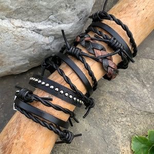 May include: A set of five black leather bracelets with silver studs. The bracelets are layered on a wooden surface.