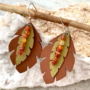May include: A pair of leather leaf earrings with a brown and green layered design. Each earring features a strand of orange and yellow beads.