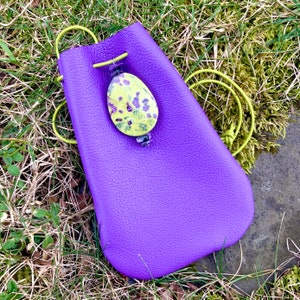 May include: A purple leather pouch with a drawstring closure. The pouch has a yellow and purple floral patterned stone attached to it.