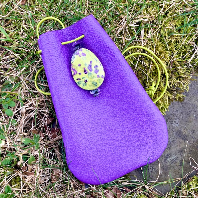 May include: A purple leather pouch with a drawstring closure. The pouch has a yellow and purple floral patterned stone attached to it.