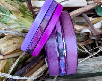 Può includere: Pila di tre braccialetti in pelle nelle tonalità del viola. Il braccialetto superiore è di un viola chiaro uniforme, quello centrale ha un motivo floreale e quello inferiore è di un viola più scuro.