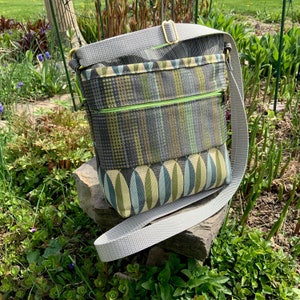 Op de afbeelding: Een grijze en groene crossbody tas met een ritsvak en een lange verstelbare schouderband.