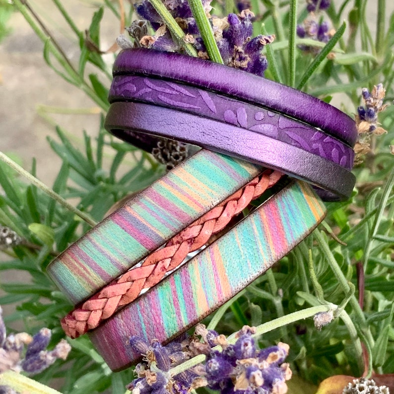 Pu&ograve; includere: Un set di tre braccialetti in pelle. Un braccialetto &egrave; viola con un motivo floreale, un altro &egrave; un braccialetto in pelle rosa intrecciato e il terzo &egrave; un braccialetto in pelle a righe multicolor.