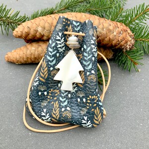 May include: A small, dark blue leather pouch with a drawstring closure. The pouch is decorated with a white and gold floral pattern. A white, tree-shaped charm hangs from the pouch.