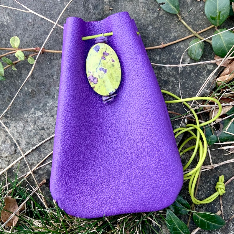 May include: A purple leather drawstring bag with a green and yellow floral patterned closure.
