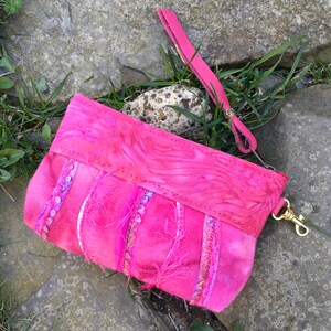 May include: A pink fabric pouch with a pink leather strap and a gold clasp. The pouch is decorated with pink and white sequins and fringe.