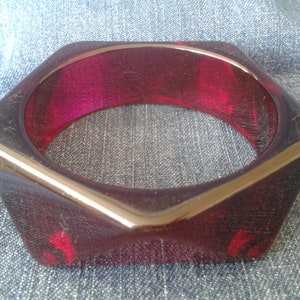 Puede incluir: Un brazalete hexagonal de plástico de color rojo oscuro.
