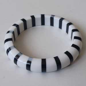 May include: A white and black striped bangle bracelet. The bracelet is made of a smooth, hard material and has a glossy finish.