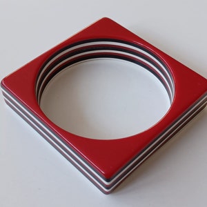 May include: Red square-shaped bangle with white and black stripes.