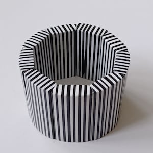 May include: A black and white striped bangle bracelet made of wood. The bracelet is made of multiple pieces of wood that are joined together to form a circle.
