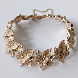 May include: A gold-tone bracelet with a chain closure and a design of interlocking leaves.
