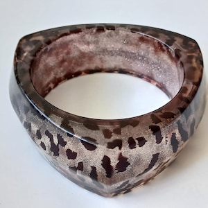 May include: A brown and white leopard print bangle bracelet with a triangular shape.