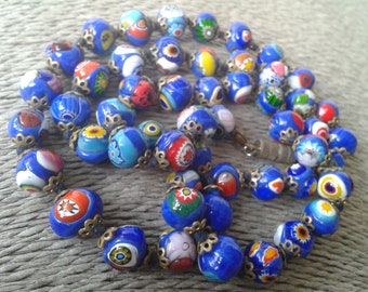 May include: A necklace made of blue glass beads with colourful patterns. The beads are strung on a silver chain with decorative metal accents.