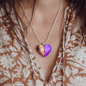 May include: A silver chain necklace with a purple and brown heart-shaped pendant. The pendant is made of resin and wood.