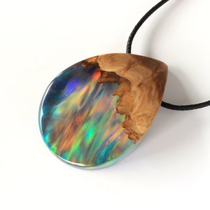 Hand holding Aurora Borealis teardrop pendant made of wood and resin, featuring red lab-grown opal with iridescent colors changing from red, green, blue, orange & more.