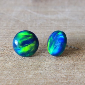 Könnte beinhalten: Ein Paar Ohrstecker mit einem Wirbelmuster aus Blau und Grün. Die Ohrringe haben eine polierte, glänzende Oberfläche und sind auf Silberstiften befestigt. Die Ohrringe sind rund und oval geformt.