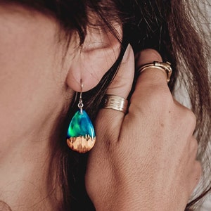 Woman wearing a teardrop green Aurora Borealis earrings made of wood, resin, and purple lab-grown opal with iridescent colors that shift from blue, green & orange.
