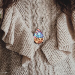 Woman wearing a large sized red Aurora Borealis pendant made of wood, resin, and lab-grown opal with iridescent colors that shift from red, green, blue, orange & more.