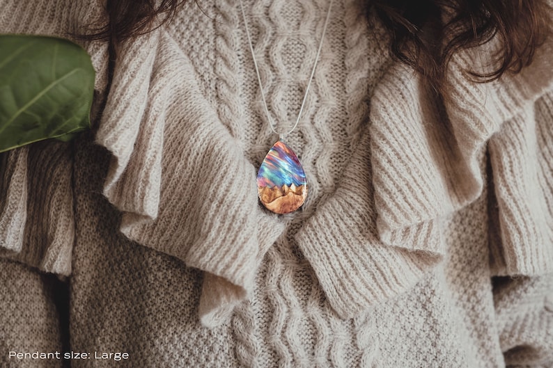 Woman wearing a large sized red Aurora Borealis pendant made of wood, resin, and lab-grown opal with iridescent colors that shift from red, green, blue, orange & more.