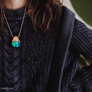 Woman wearing a sized Aurora Borealis pendant made of wood, resin, and green lab-grown opal with iridescent colors that shift from blue, green & orange.