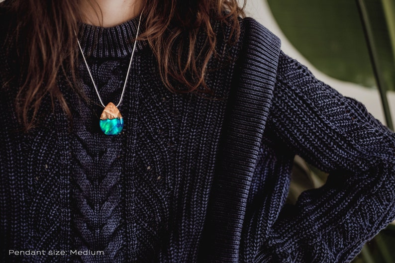 Woman wearing a sized Aurora Borealis pendant made of wood, resin, and green lab-grown opal with iridescent colors that shift from blue, green & orange.