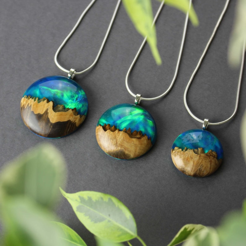 Three wood and resin round pendants of varying sizes - small, medium and large, each featuring green lab-grown opal with iridescent colors changing from blue, green & orange.