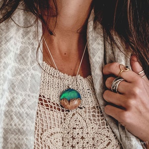 Woman wearing a medium sized Aurora Borealis pendant made of wood, resin, and green lab-grown opal with iridescent colors that shift from blue, green & orange.