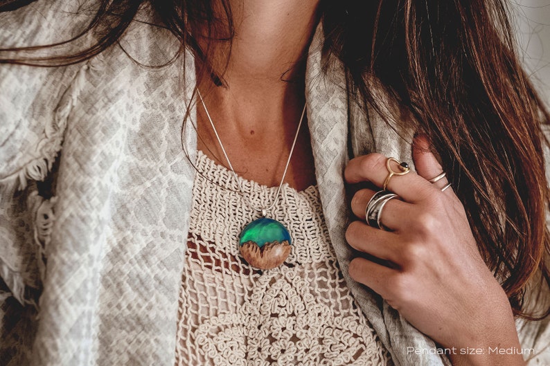 Woman wearing a medium sized Aurora Borealis pendant made of wood, resin, and green lab-grown opal with iridescent colors that shift from blue, green & orange.