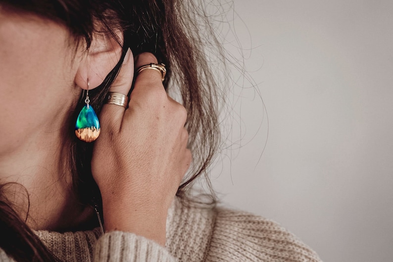 Woman wearing a teardrop green Aurora Borealis earrings made of wood, resin, and purple lab-grown opal with iridescent colors that shift from blue, green & orange.