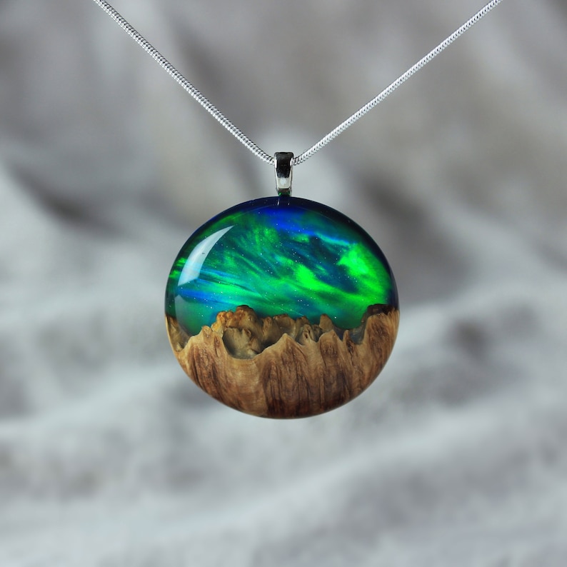 Round pendant handmade with green lab-created opal, burl wood and resin. Opals iridescent colors resemble aurora borealis in motion and the burl wood texture gives the impression of a mountain peaks.