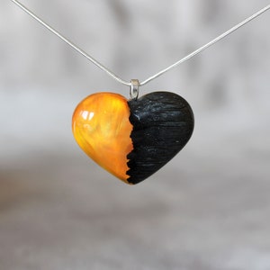 May include: A heart-shaped pendant necklace with a black and orange resin design. The pendant is made of two halves, one black and one orange, with a smooth, polished finish.