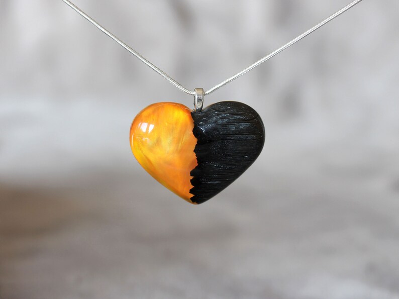 May include: A heart-shaped pendant necklace with a black and orange resin design. The pendant is made of two halves, one black and one orange, with a smooth, polished finish.
